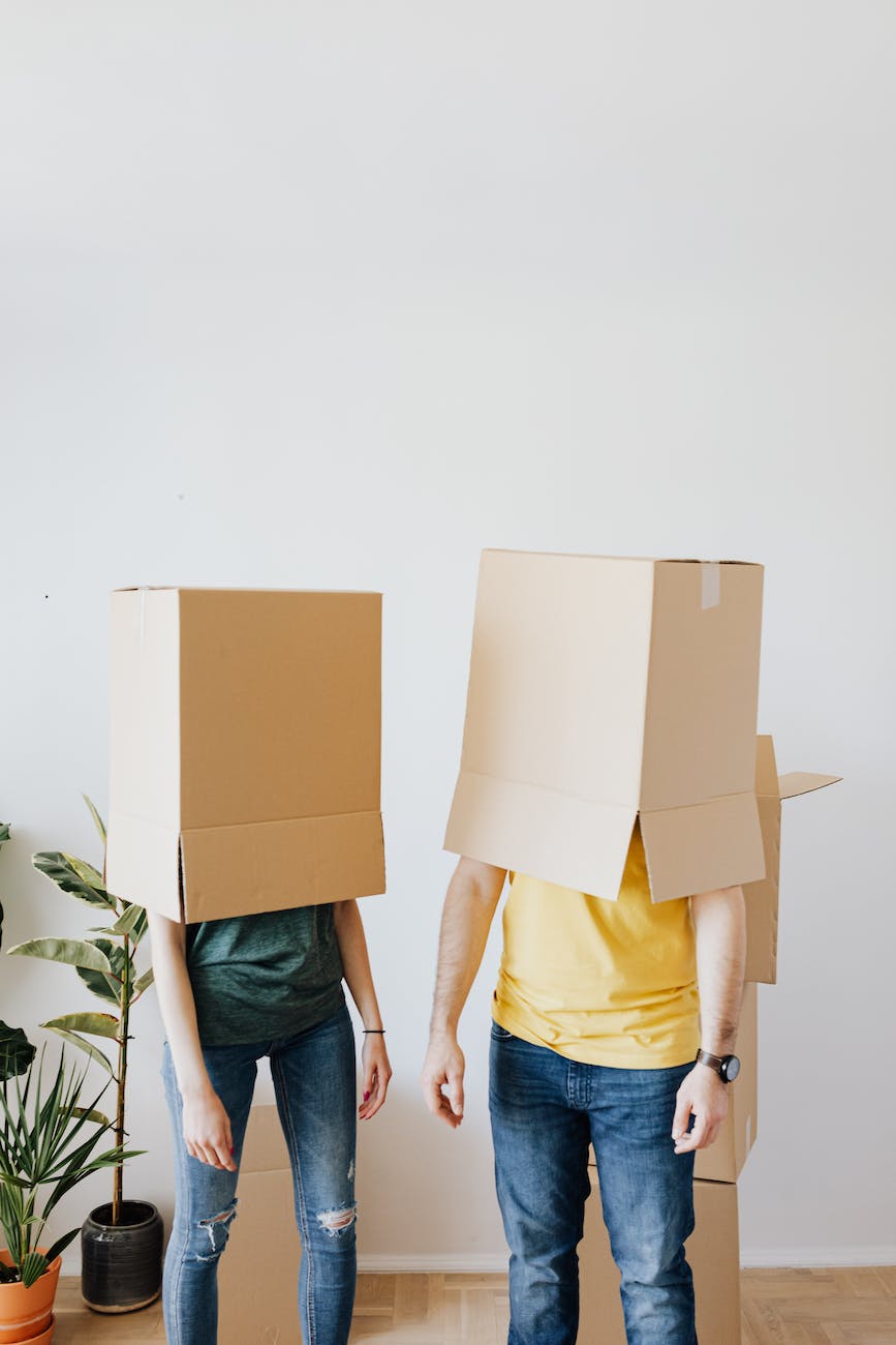 unrecognizable couple carrying carton boxes on heads